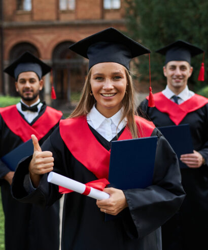 Graduate female shows like with her friends in graduation gowns holding diploma and smiling at camera.