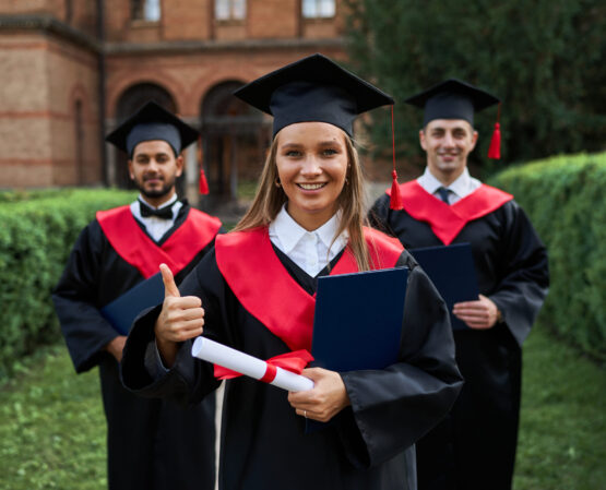 Graduate female shows like with her friends in graduation gowns holding diploma and smiling at camera.